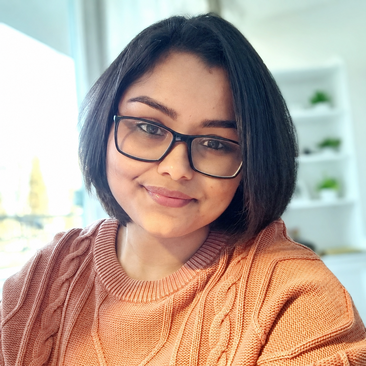 Portrait of Suvra Nath wearing glasses and an orange sweater.